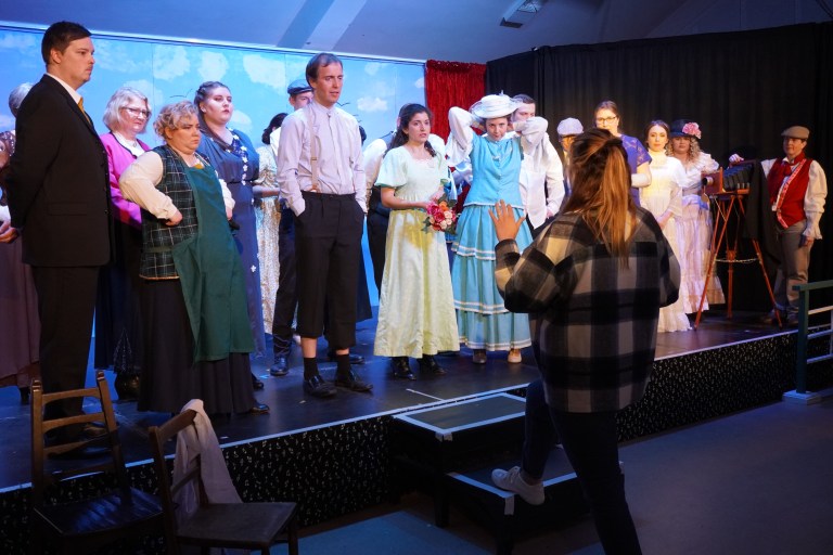 The cast being addressed by the director during rehearsals